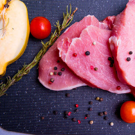 Pork. Fresh pork steaks on a black chopping board and spiced, cherry tomatoes, rosemary,...