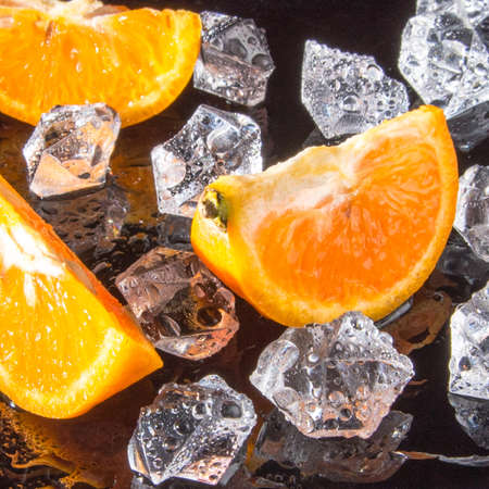Tangerine slices with ice drops on a black background, close-up, background, template, still lifeの写真素材