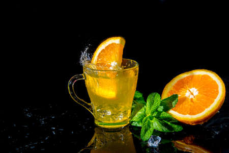 Splashes in a glass with orange juice and mint orange halves on a black background, Healthy...