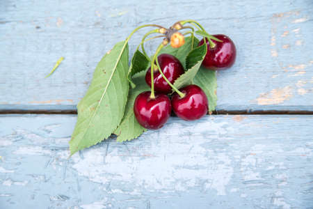 Red cherry green leaves on light blue wood table, copy spaceの写真素材