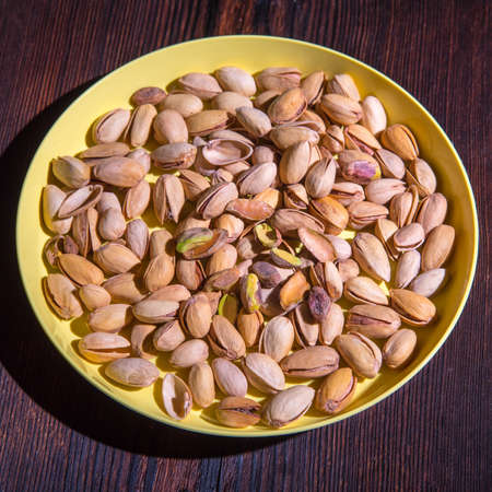 Pistachio nuts in a yellow bowl on a wooden background, side view, copy spaceの写真素材