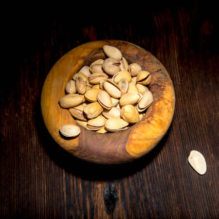 Pistachio nuts in a wooden bowl on a wooden background, side view, copy spaceの写真素材