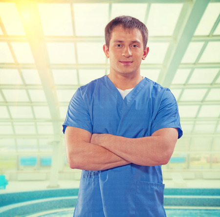 handsome young doctor with crossed arms looking at camera on background of big window の写真素材