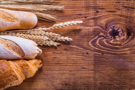 baguettes and croissant with wheat ears on old wooden boardの写真素材