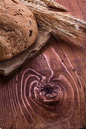 loaf of bread and wheat ears om old wooden boardの写真素材