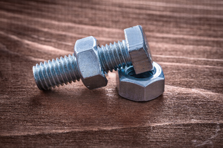 Threaded metal bolt and some screw nuts on vintage wooden board