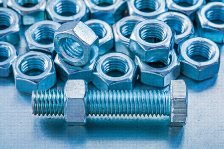 Close up version of stainless screw nuts and bolts on metallic b