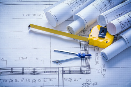 rolled blueprints compass and yellow tapeline.