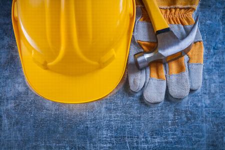 Safety gloves yellow building helmet and claw hammer on scratched metallic background maintenance...