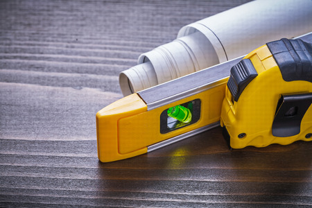Measuring tape blueprints and construction level on vintage wooden board close up view maintenance...