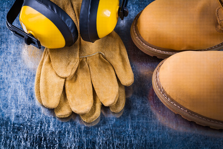 Set of safety boots leather gloves and noise reduction headphones on scratched metallic surface construction concept.の写真素材