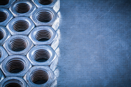 Collection of threaded screw-nuts on scratched metallic background construction concept.