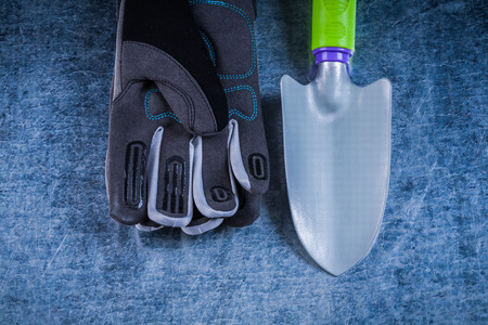 Set of metal spade fabric gloves on scratched metallic surface.