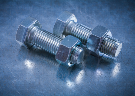 Composition of threaded bolts and construction nuts on metallic background.