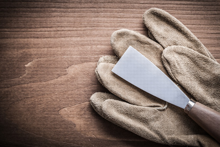 paint scraper and safety glove on wooden board.
