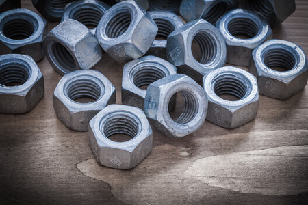 Heap of steel threaded construction nuts on vintage wooden surface.