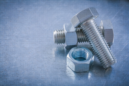 Stainless threaded bolts screw-nuts on scratched metallic background maintenance concept.