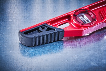 Red construction level on scratched metallic background maintenance concept.