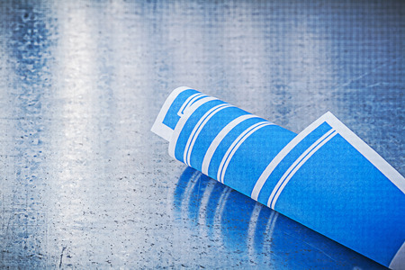 Blue rolled up construction plans on scratched metallic background.