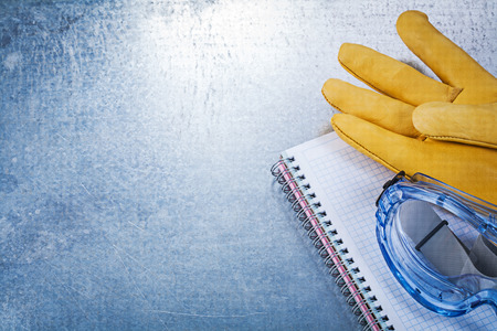Safety glasses gloves copybook on metallic background.