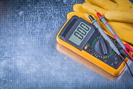 Digital electrical tester safety gloves on metallic background electricity concept.
