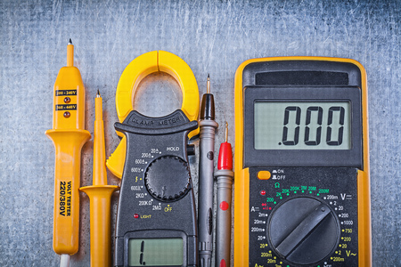 Digital clamp meter electrical tester multimeter on metallic background electricity concept.