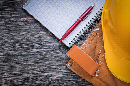 Toolbelt building helmet checked notepad ball-point pen on wooden board construction concept.の写真素材