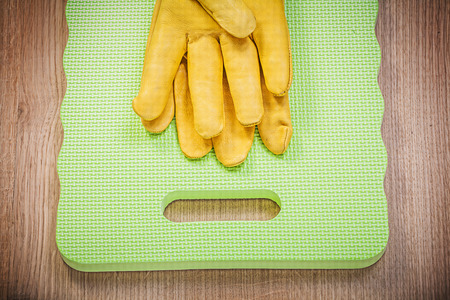 Pair of yellow protective leather gloves foam garden knee mat on wooden board gardening concept.の写真素材