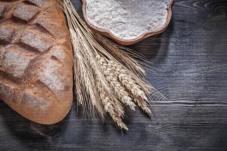 Loaf of brown bread wheat rye ears wooden bowl with flour on wood board.の写真素材