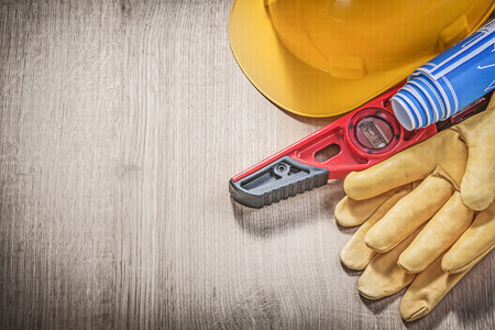 Hard hat protective gloves construction level blue rolled up engineering drawings on wooden board.