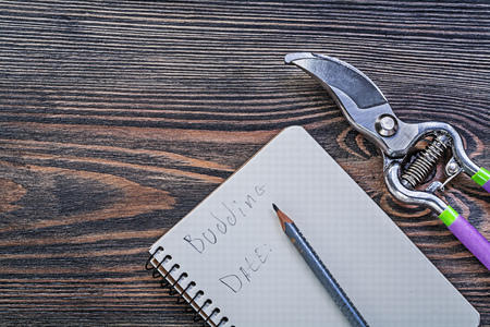 Notepad pencil garden pruner on vintage wooden board gardening concept.