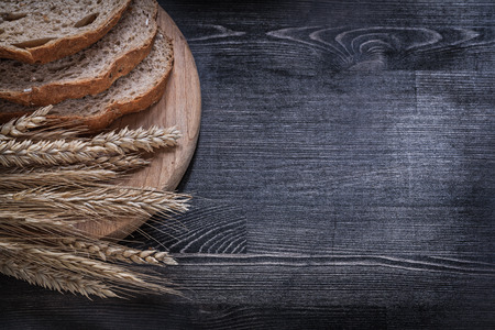 Sliced brown bread on wooden chopping board wheat rye ears copy space.
