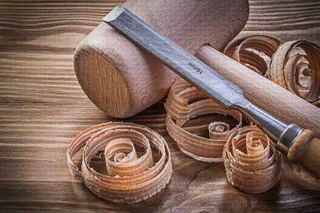 Wooden mallet flat chisels planning chips on vintage wood board construction concept.