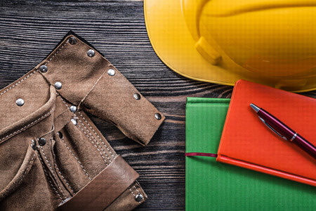 Composition of tool belt note-books pen building helmet on wooden board construction concept.