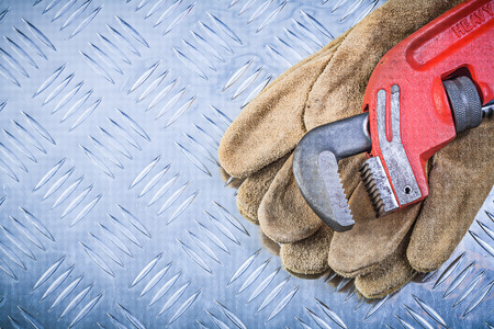 Leather protective gloves pipe wrench on channeled metal background construction concept.