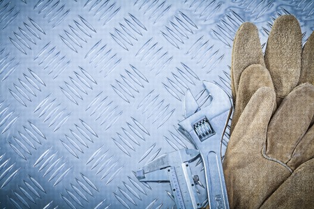 Leather safety gloves slide caliper monkey spanner on corrugated metal sheet construction concept.