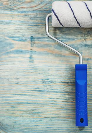 Paint roller on wooden board close up view construction concept.