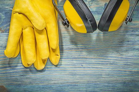 Pair of leather safety gloves noise reduction earmuffs on wooden board construction concept.