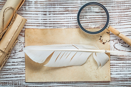 Old sheet corded paper roll feather magnifying glass on vintage wooden board.の写真素材