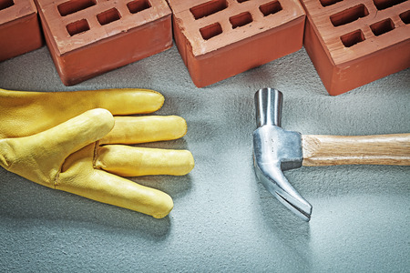 Red bricks leather safety gloves claw hammer on concrete background building concept.