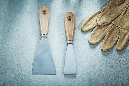 Putty knife pair of leather safety gloves on concrete surface construction concept.