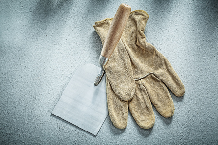 Stainless putty knife leather protective glove on concrete background construction concept.