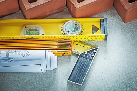 Red bricks construction level wooden meter blueprints square ruler on concrete surface building...