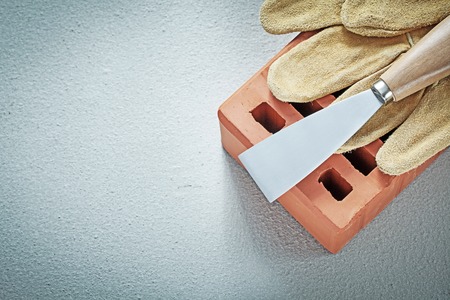Red bricks leather protective gloves putty spattle on concrete background bricklaying concept.の写真素材
