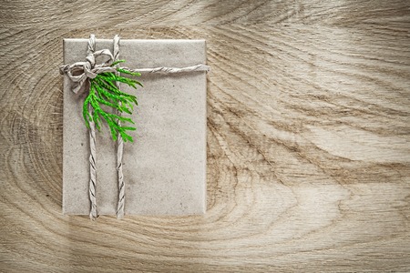 Handmade present box wrapped in brown paper with green branch on wooden board.の写真素材