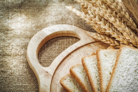 Chopping board sliced bread wheat ears on sacking background.の写真素材