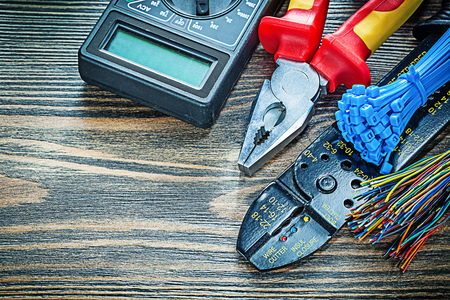 Electric tester wires cable ties bolt cutter pliers voltmeter on wooden board.