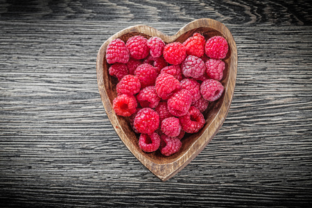 Heart-shaped bowl with raspberries on wooden board.の写真素材