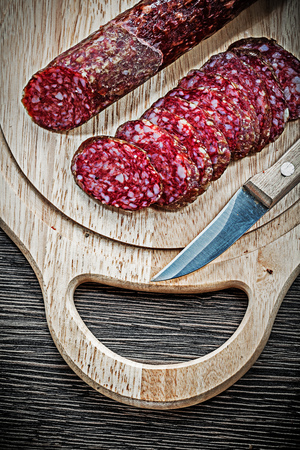 Sliced salami and knife on wooden chopping board.の写真素材