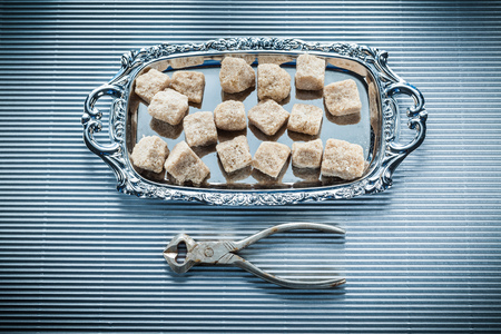 Brown sugar cubes pliers tray on striped background.の写真素材